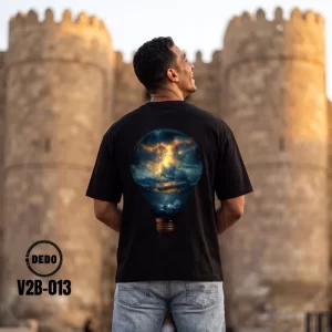 DEDO V2B-013 black oversized t-shirt in front of a historic stone fortress, highlighting the vibrant back graphic of an electric storm and ocean inside a lightbulb.