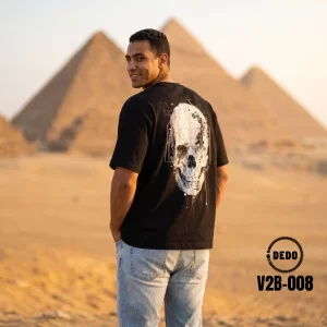 Man wearing a black DEDO T-shirt with an artistic skull design in front of the Giza Pyramids