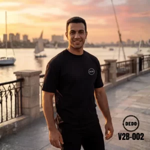 DEDO V2B-002 black oversized T-shirt with minimalist chest logo by the waterfront at sunset